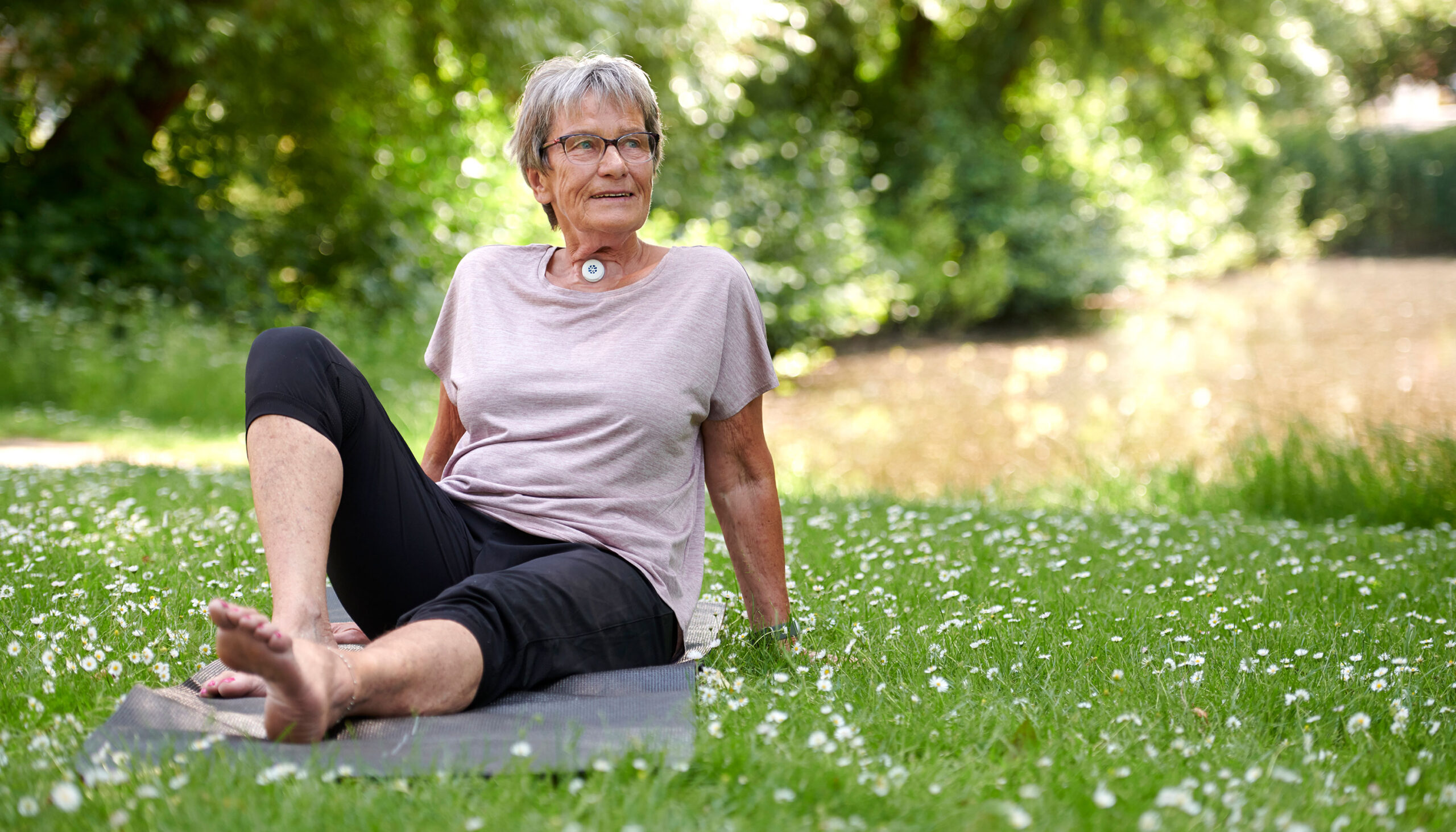 Woman with a necj stoma using Provox HME while exercising yoga outdoors.